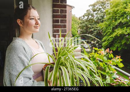 Contemplative teenage girl with potted spider plant on balcony Stock Photo