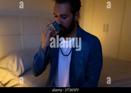 Man using inhaler sitting on bed at home Stock Photo