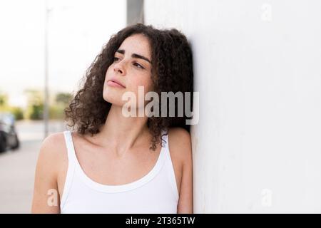 Thoughtful young woman leaning on wall Stock Photo