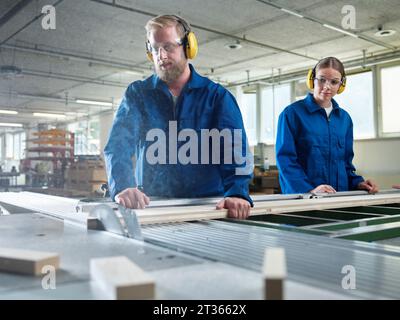 Carpenter sawing wooden plank in factory Stock Photo