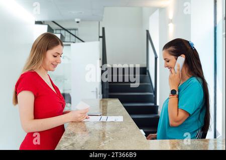 Receptionist talking on smart phone by patient at checkout in clinic Stock Photo