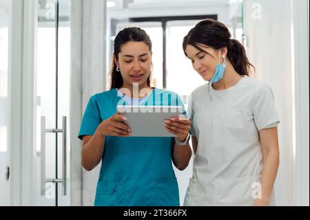 Smiling dentist using tablet PC by colleague in corridor Stock Photo