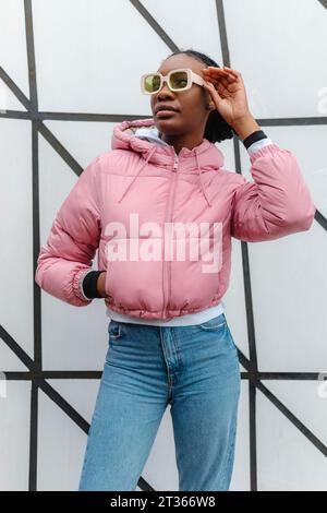 Young woman wearing sunglasses standing in front of wall Stock Photo