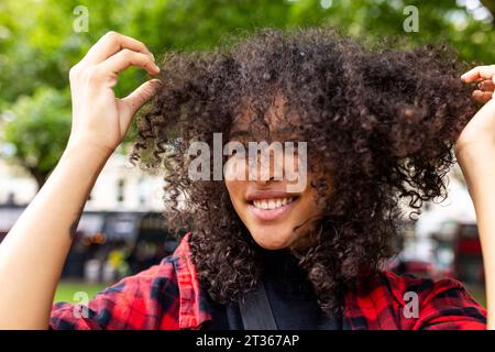Smiling woman playing with hair in park Stock Photo