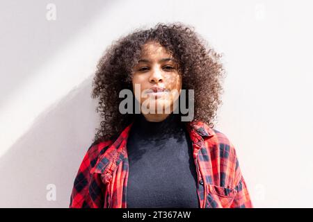 Smiling woman with curly hair in front of wall Stock Photo