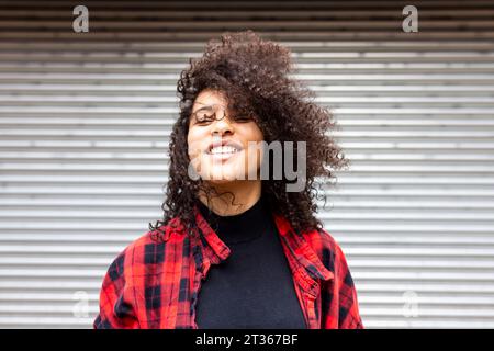 Smiling woman with curly hair in front of shutter Stock Photo