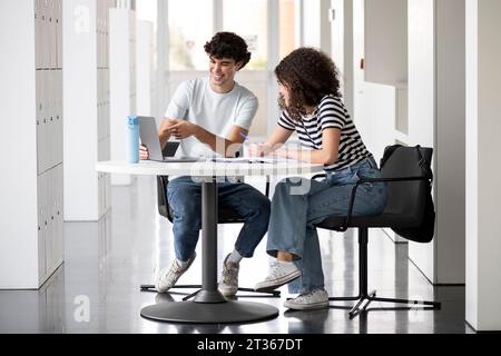 Happy students studying and discussing over laptop at table in university Stock Photo