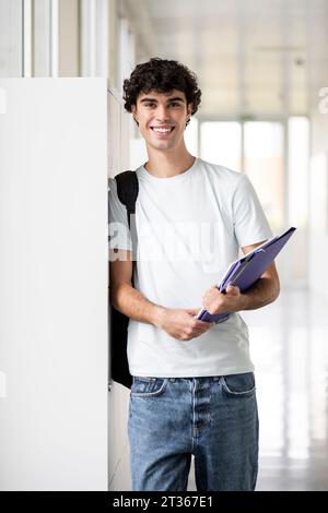 Smiling student with backpack and file folder standing in corridor Stock Photo