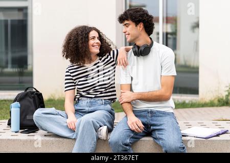 Smiling students sitting on concrete bench in front of building Stock Photo