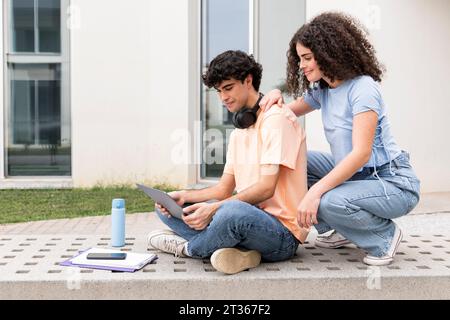 Smiling students using laptop on concrete bench in campus Stock Photo