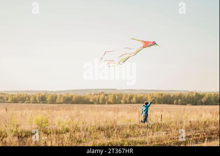 Playful boy flying kite in field Stock Photo