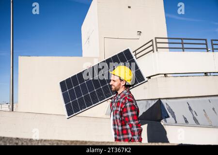 Engineer wearing hardhat carrying solar panel on shoulder Stock Photo
