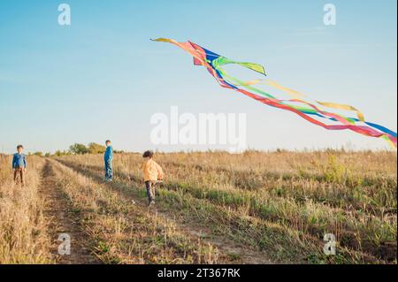 Father and sons flying kite in field on sunny day Stock Photo