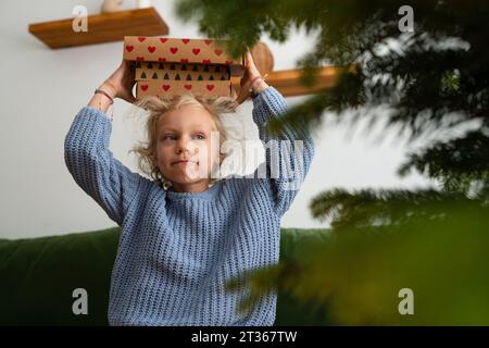 Blond girl carrying Christmas presents on head at home Stock Photo