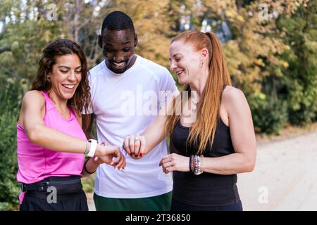 Happy friends using smart watch standing at park Stock Photo