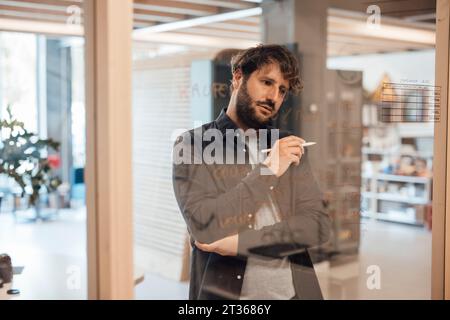 Thoughtful businessman writing on glass wall at office Stock Photo