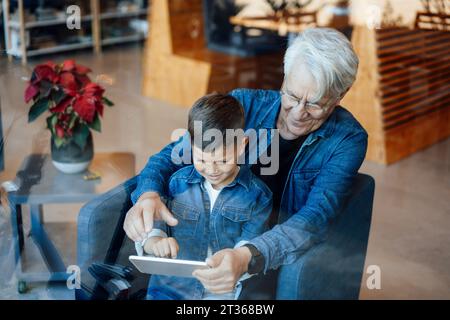 Boy using tablet PC sitting with grandfather at home Stock Photo