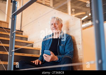 Thoughtful senior man holding smart phone at home Stock Photo