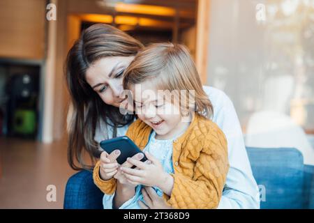 Happy daughter using smart phone with mother at home Stock Photo