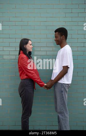 Loving couple holding hands standing in front of brick wall Stock Photo