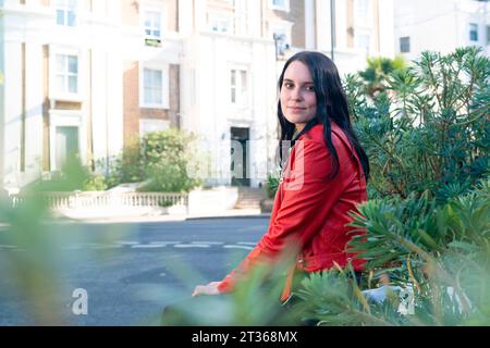 Smiling young woman sitting near plants Stock Photo