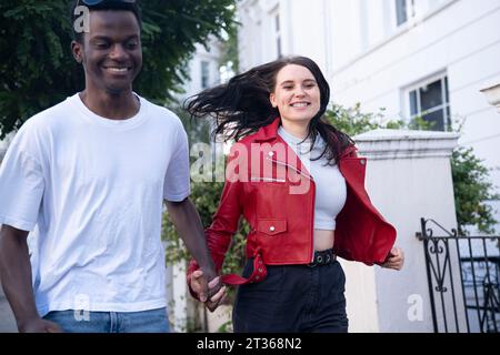 Happy young couple holding hands and running near building Stock Photo