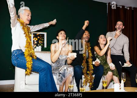 Happy multi-generation family cheering on sofa while celebrating new year at home Stock Photo
