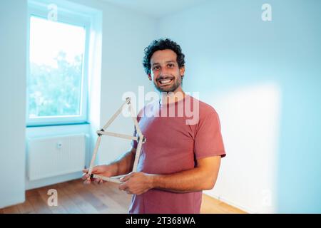 Smiling man standing with model house at home Stock Photo