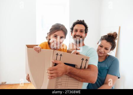 Happy man and woman with daughter sitting in cardboard box at home Stock Photo