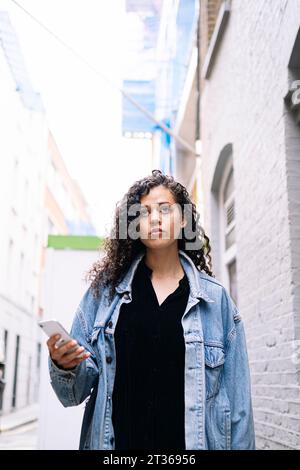 Contemplative young woman standing with smart phone Stock Photo