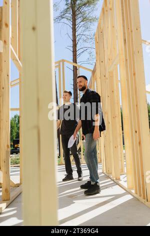 Engineers standing with blueprint near construction frame on sunny day Stock Photo