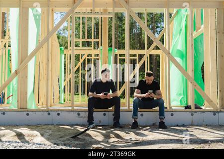 Engineers using smart phone sitting at construction site Stock Photo