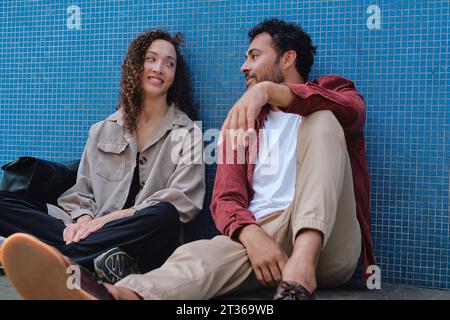 Happy couple sitting together near blue wall Stock Photo