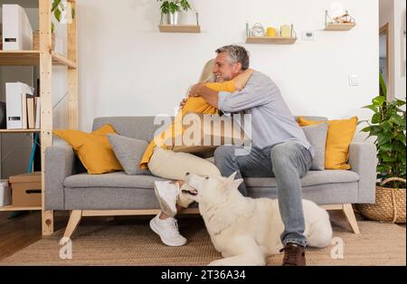 Happy couple embracing each other sitting on sofa by dog at home Stock Photo