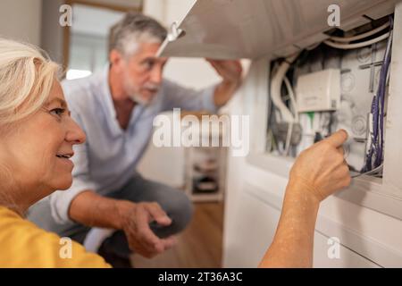Woman examining electrical cable in fuse box with man at home Stock Photo