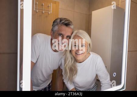 Reflection of happy man and woman in illuminated mirror at home Stock Photo
