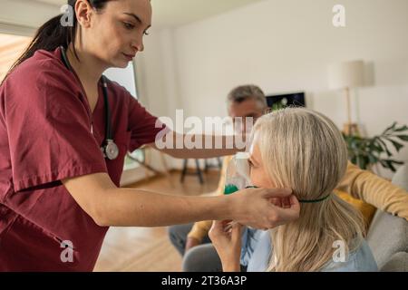 Doctor helping patient wearing oxygen mask at home Stock Photo