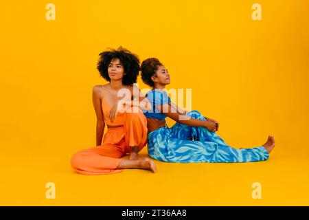 Young friends sitting together against yellow background Stock Photo