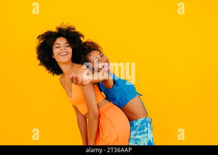 Carefree woman leaning on friend against yellow background Stock Photo
