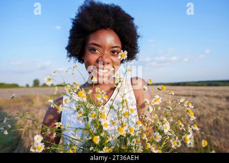 Smiling woman holding bunch of daises in field on sunny day Stock Photo