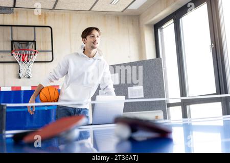 Smiling young trainee standing with basketball in office Stock Photo