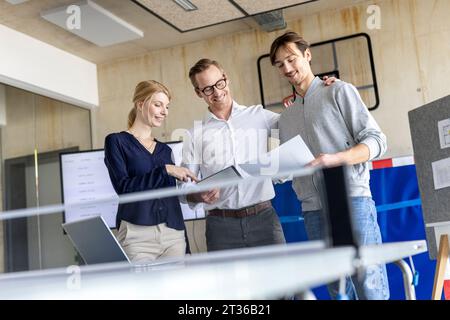 Smiling businessman discussing over document with colleagues in modern office Stock Photo