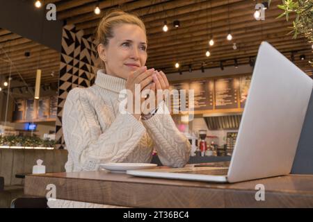 Thoughtful businesswoman with laptop having coffee at cafe Stock Photo
