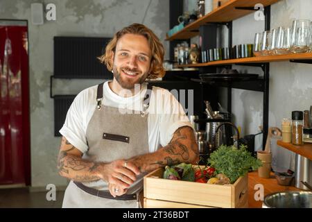 Smiling owner leaning on vegetable crate in store Stock Photo