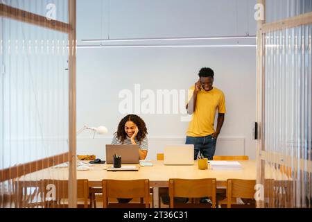 Smiling student using laptop with friend talking on smart phone Stock Photo