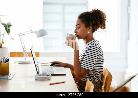 Young student drinking coffee and using laptop at desk Stock Photo
