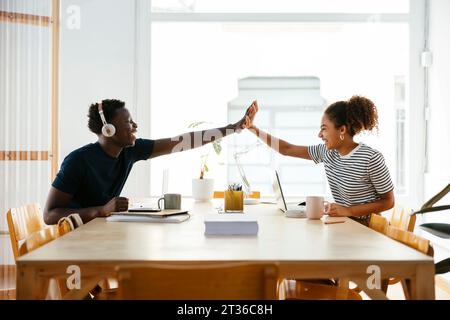 Happy young students giving high-five to each other at desk Stock Photo