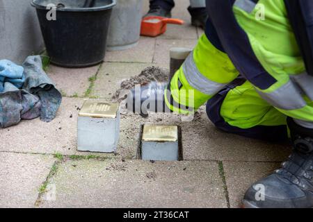 Wiesbaden, Germany - October 17, 2023: A bricklayer lays Stolpersteine on a pavement in the city center of Wiesbaden, Germany. A Stolperstein (literally 'stumbling stone') is a concrete cube provided with a brass plate inscribed with the name and life dates of victims of Nazi extermination. Stock Photo