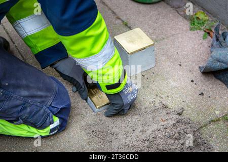 Wiesbaden, Germany - October 17, 2023: A bricklayer lays Stolpersteine on a pavement in the city center of Wiesbaden, Germany. A Stolperstein (literally 'stumbling stone') is a concrete cube provided with a brass plate inscribed with the name and life dates of victims of Nazi extermination. Stock Photo