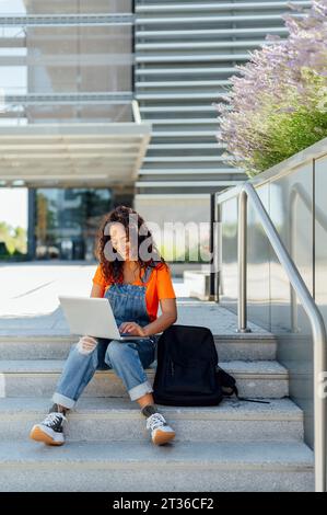 Happy student using laptop sitting on steps in campus Stock Photo